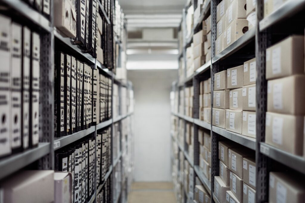 Scaffalature di un archivio con faldoni numerati allineati lungo un corridoio stretto