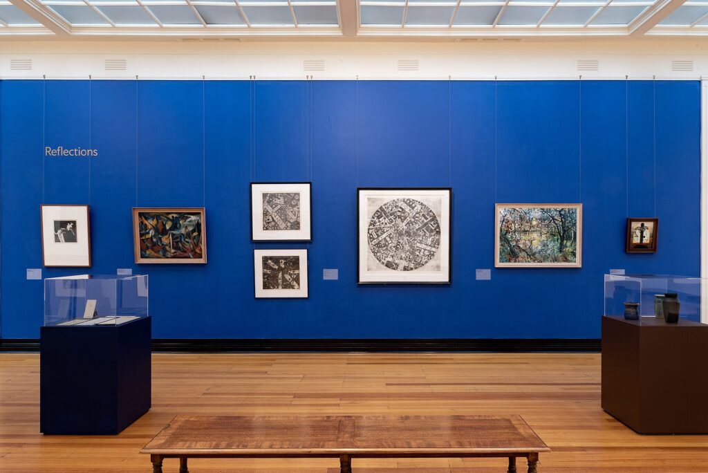 Parete di una galleria d'arte con dipinti incorniciati illuminati da faretti orientabili