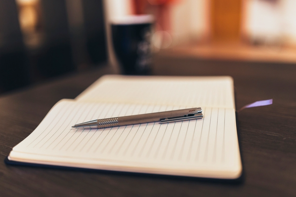 Quaderno aperto con una penna appoggiata sopra su una scrivania in penombra