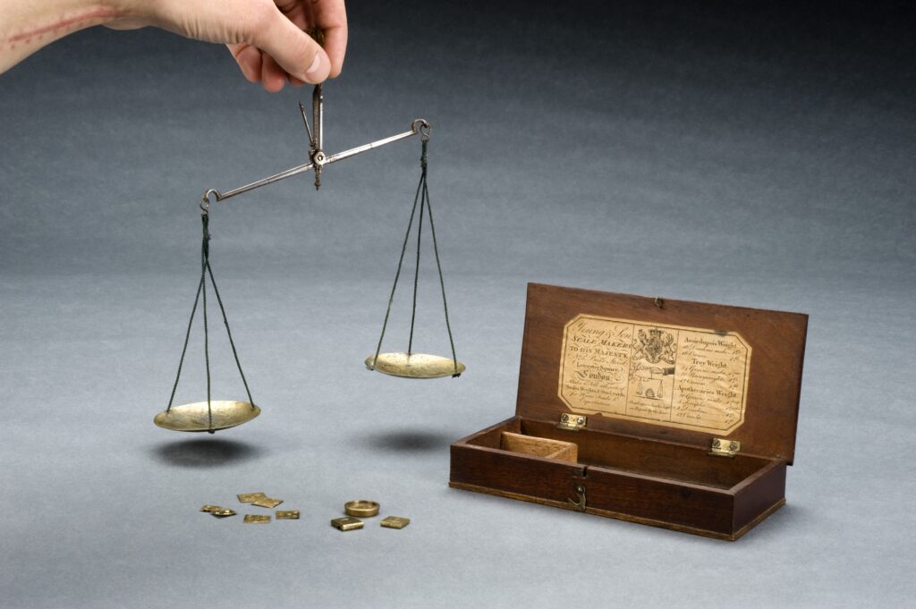 Bilancia a due piatti in ottone con una serie di pesi allineati sul ripiano di legno