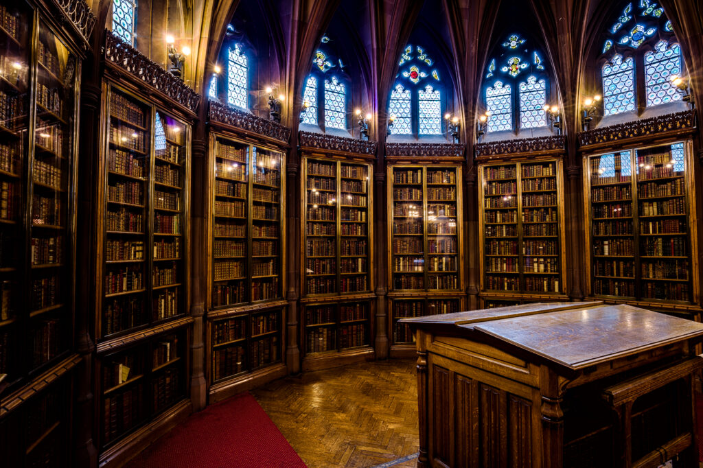 Sala di lettura di una biblioteca con tavoli lunghi e scaffali pieni di volumi